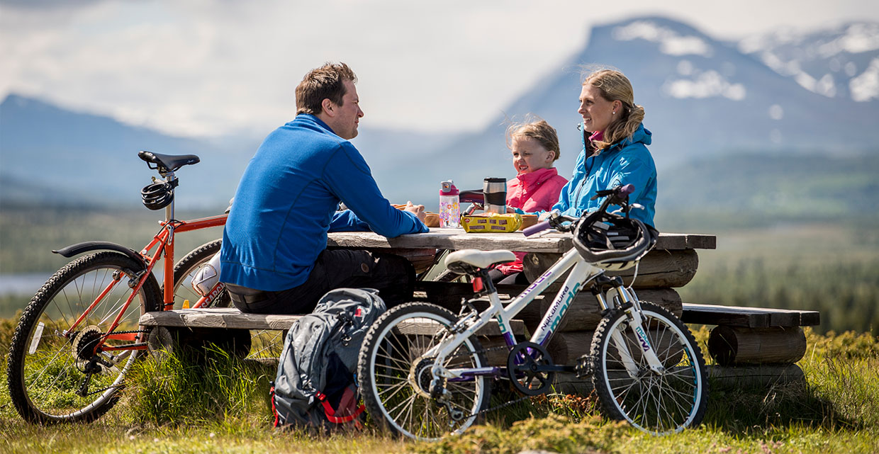 Familie med sykler sitter ved rastebenk