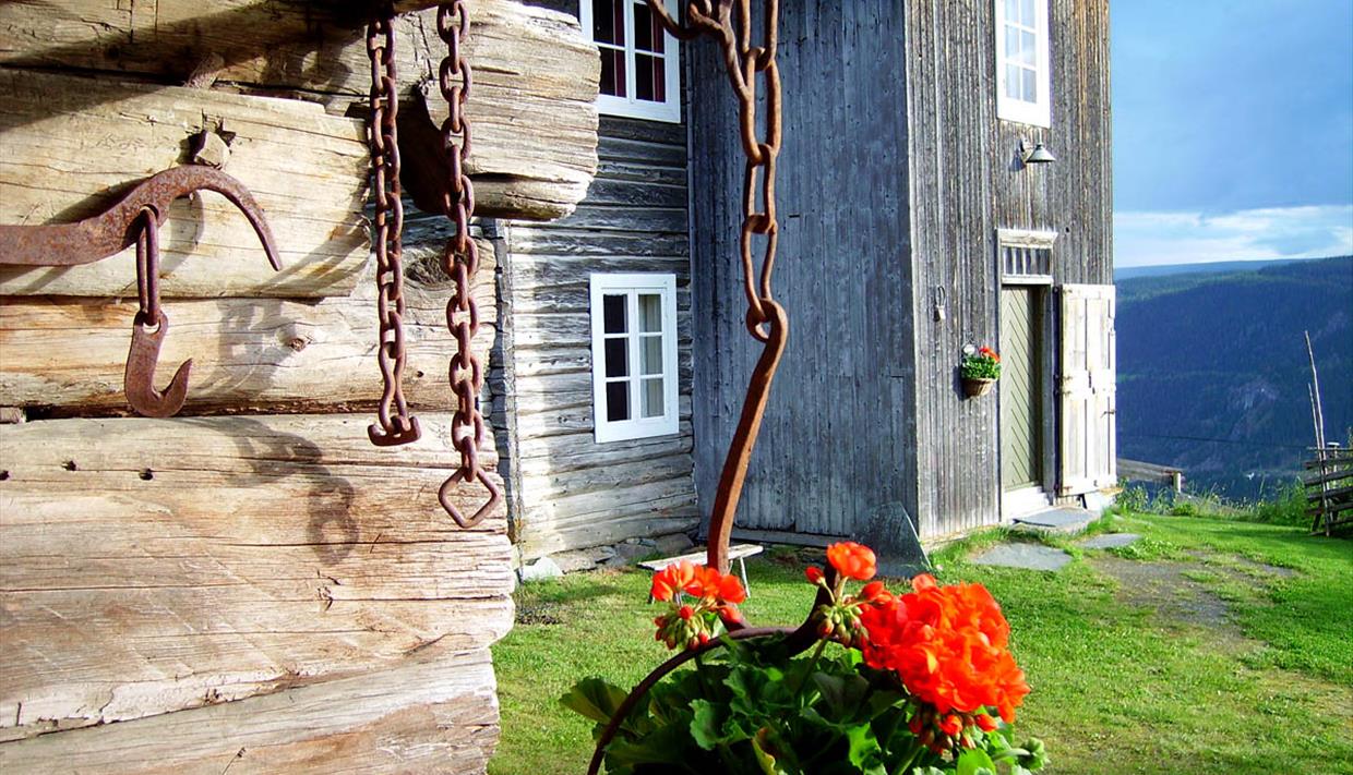 Gammelt trehus med blomster utenfor og flott utsikt over dalføret.