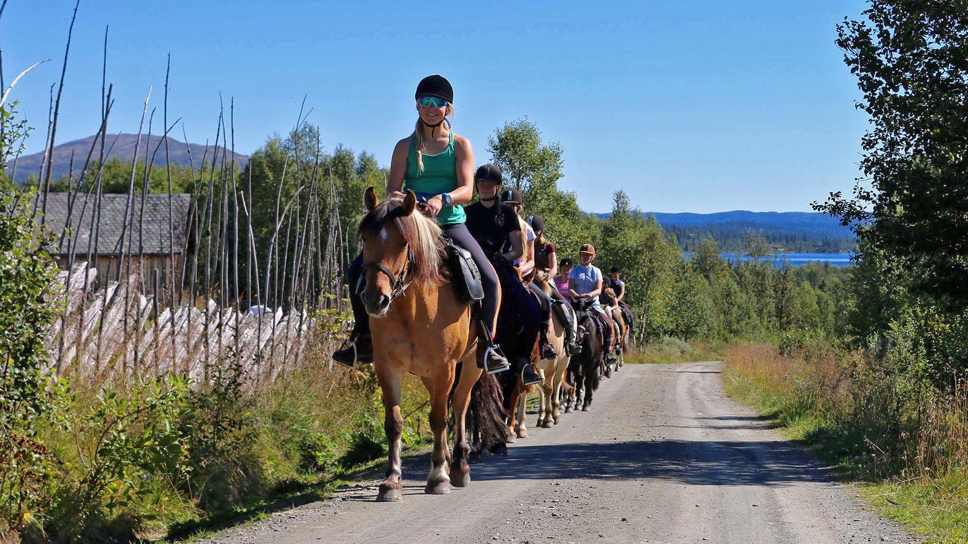 Ryttere langs en stølsveg med skigard og et vann i bakgrunnen