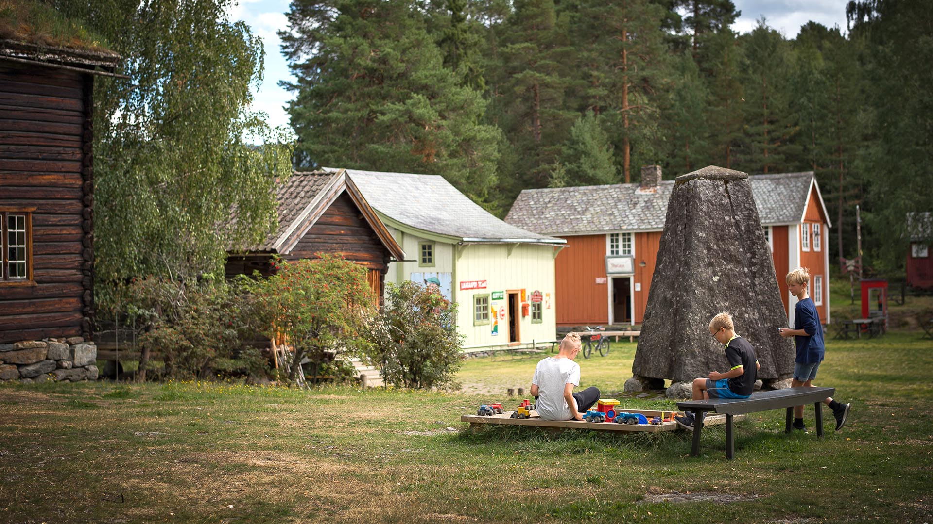 Barn på lekeplassen på plenen ute på Valdres Folkemuseum med gamle hus rundt.